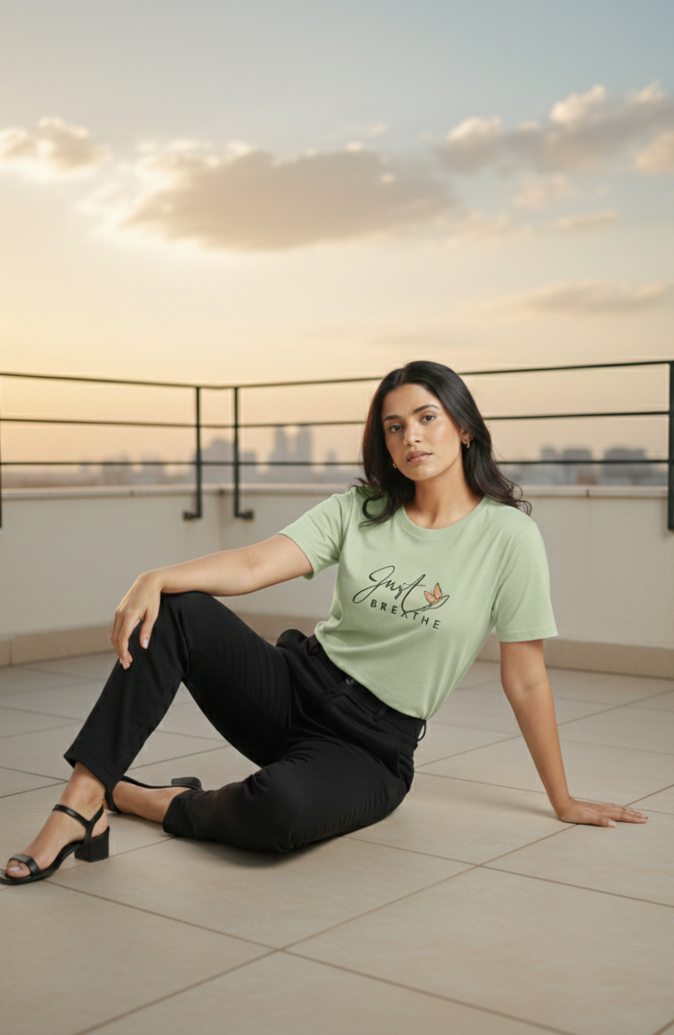 Woman sitting on a rooftop with a cityscape in the background wearing a light green t-shirt.